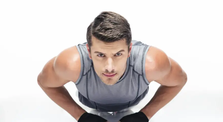 Hombre concentrado haciendo diamond push ups, con guantes negros y camiseta gris.
