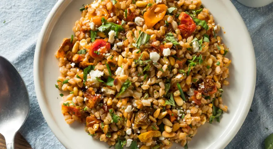 Ensalada de farro que es un plato mediterráneo con tomates secos, piñones y queso feta desmenuzado, todo mezclado con granos de farro.