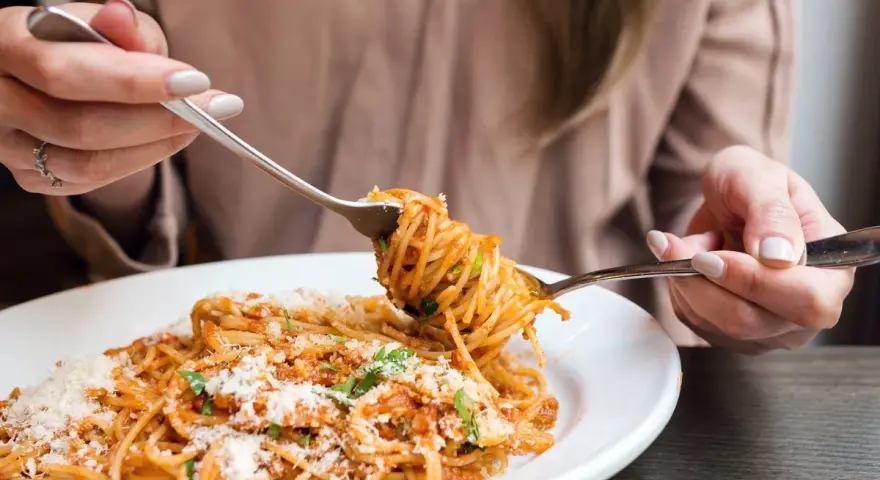 Mujer disfrutando un plato de pasta integral con salsa boloñesa y queso rallado. ¡Cuidado, la pasta integral engorda si no se consume con moderación!