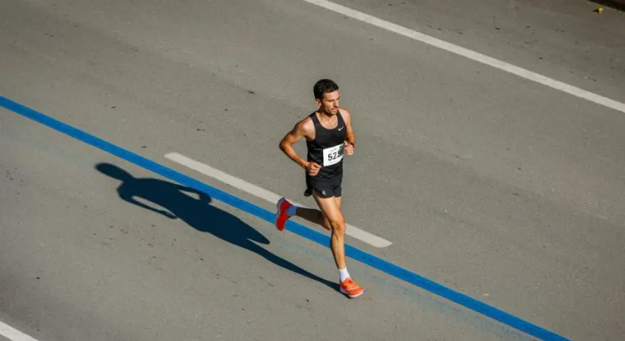 Corredor concentrado en la carrera, aprendiendo como respirar al correr para optimizar su rendimiento. Su sombra se proyecta larga sobre el asfalto.