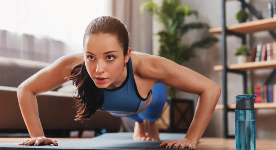 Mujer concentrada haciendo flexiones, parte de sus ejercicios de fuerza en casa.