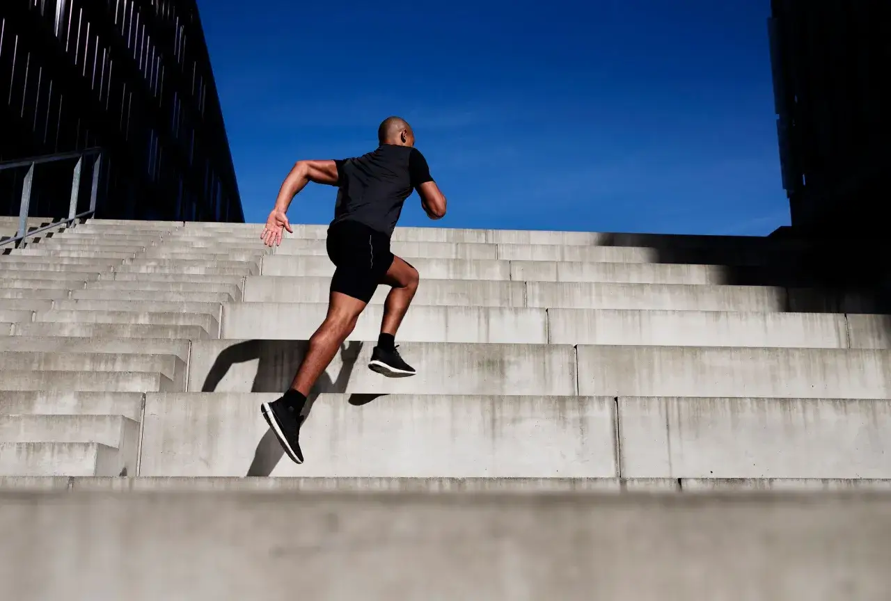 Hombre corre escaleras arriba, disfrutando de los subir escaleras beneficios. Cielo azul y arquitectura moderna.
