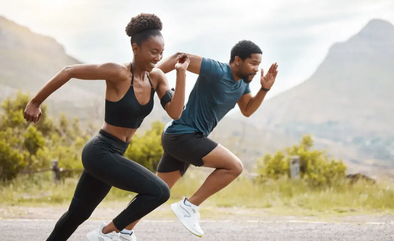 Pareja corriendo enérgicamente, practicando ejercicios pliométricos para corredores en un paisaje montañoso.