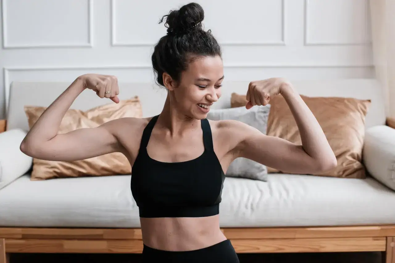 Mujer sonriente mostrando sus bíceps, un ejemplo de cuáles son los ejercicios de fuerza.