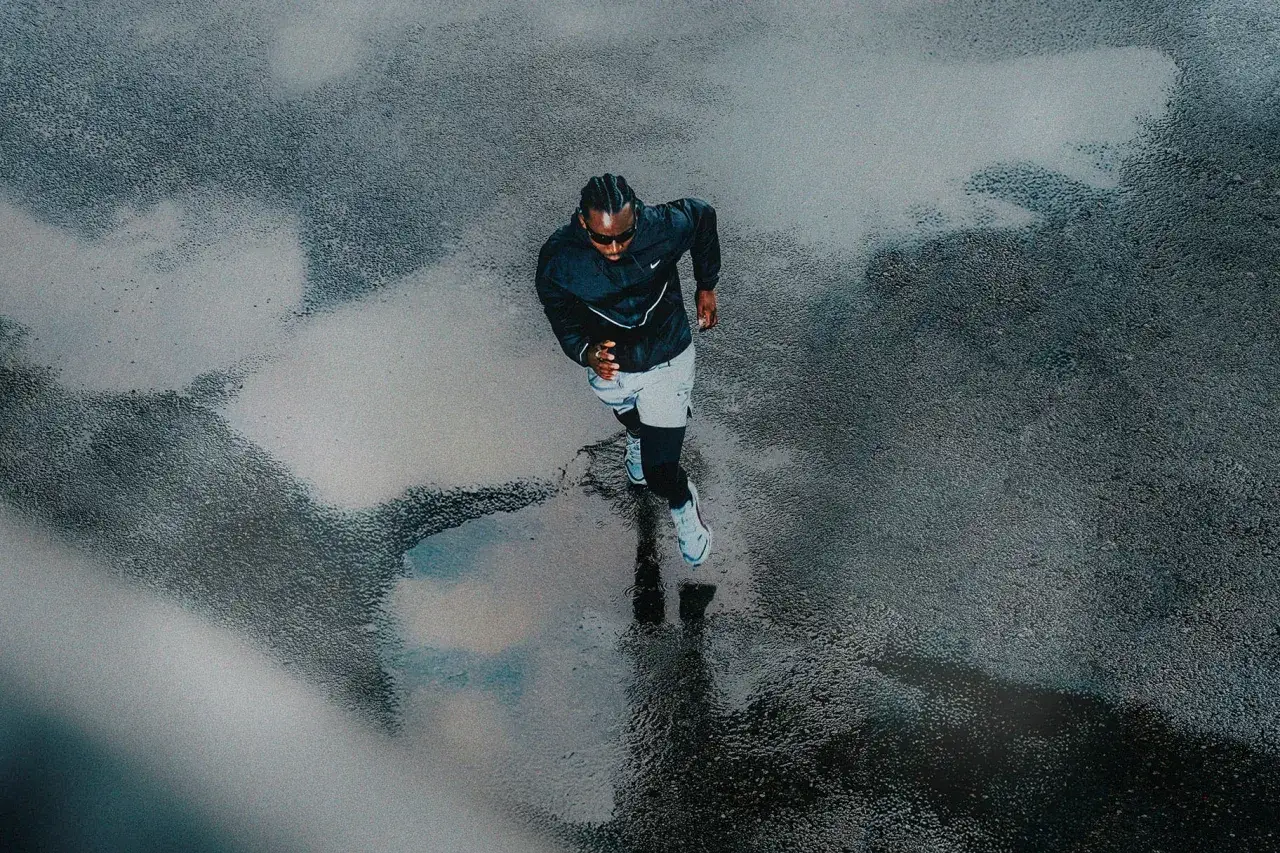 Hombre corre con lluvia, su sombra se refleja en el asfalto mojado.