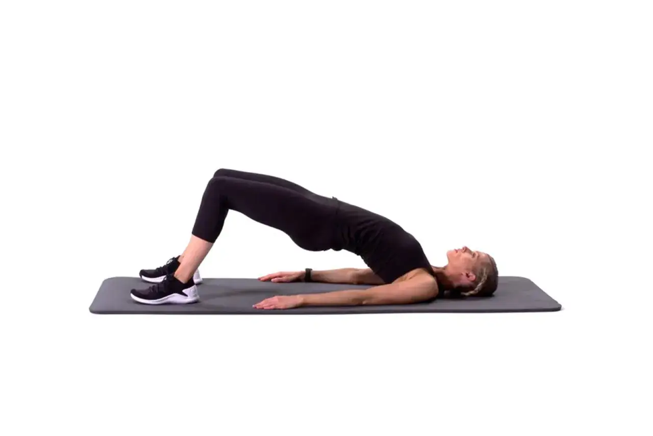 Mujer realizando un glute bridge hold en una esterilla, con las rodillas flexionadas y la cadera elevada.