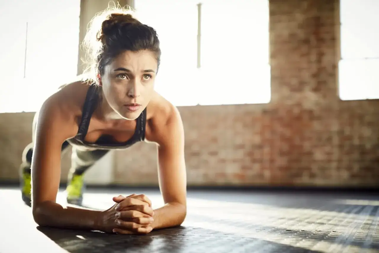 Mujer concentrada haciendo plancha, parte de sus ejercicios de fuerza en casa para mujeres.