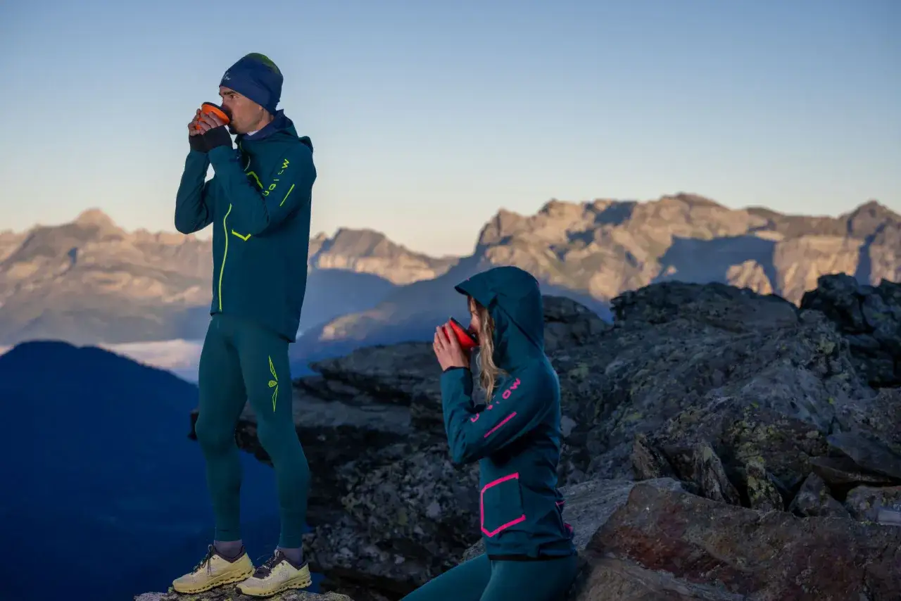 Pareja disfrutando de una bebida caliente en la cima de una montaña, luciendo ropa de correr de invierno.