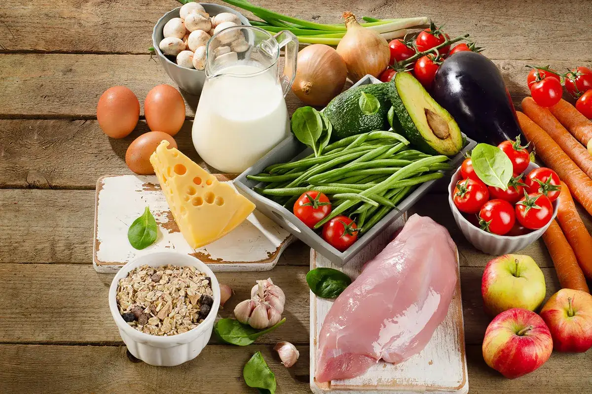 Variedad de alimentos con hierro: pollo, huevos, espinacas, brócoli, lentejas, frutos secos, cereales y frutas.