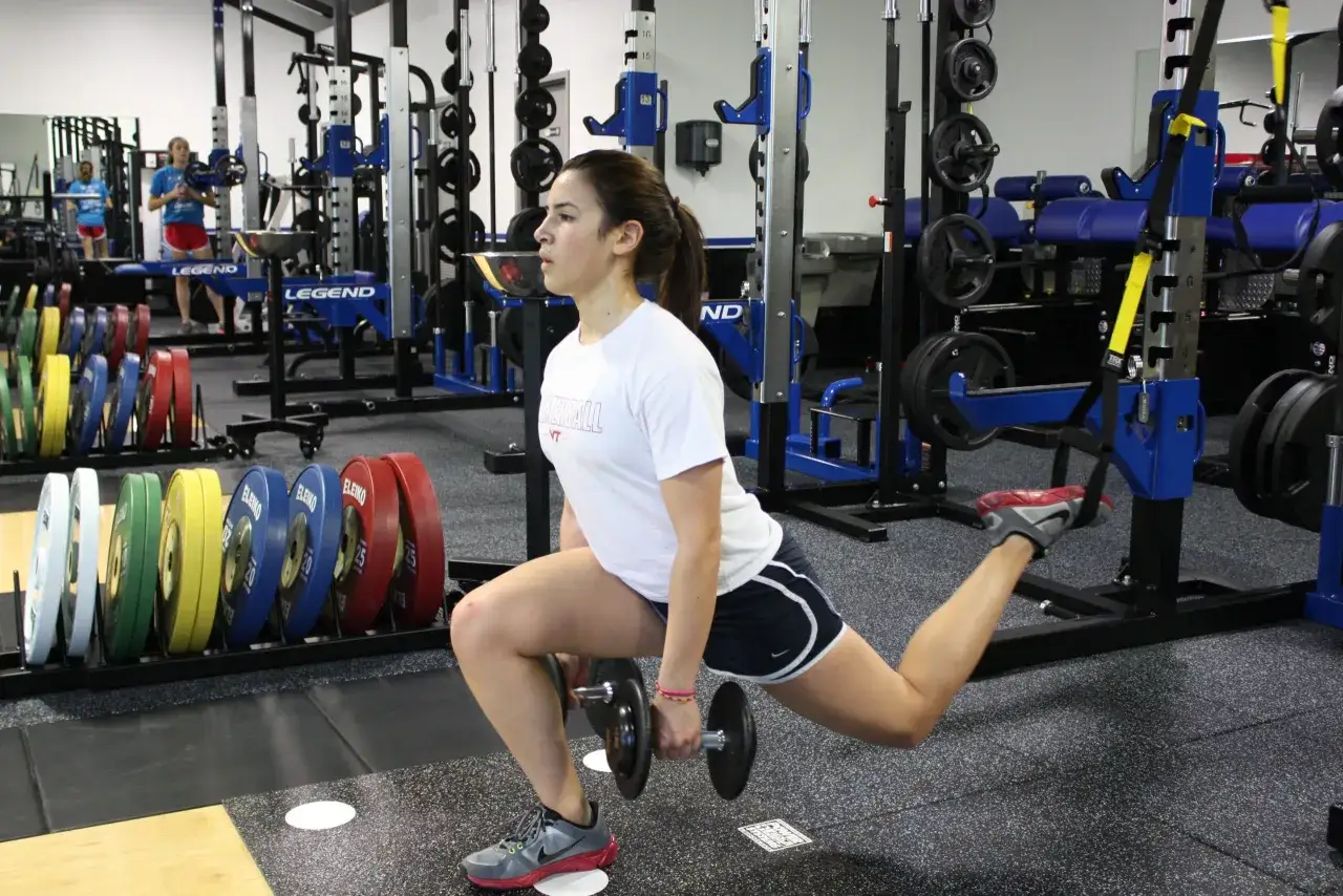 Mujer haciendo zancadas b&uacute;lgaras con mancuernas en un gimnasio, entrenando como Mijailo Mudryk.