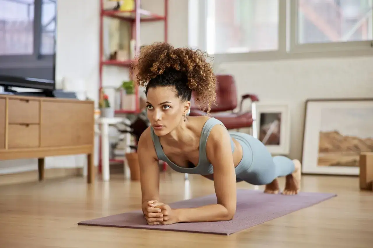 Mujer haciendo plancha, un ejercicio clave para perder barriga y cintura, en su sala de estar.
