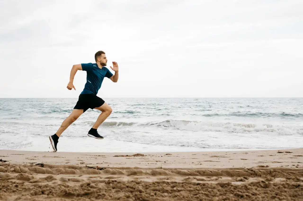 Hombre corriendo en la playa, con el mar y el cielo de fondo.