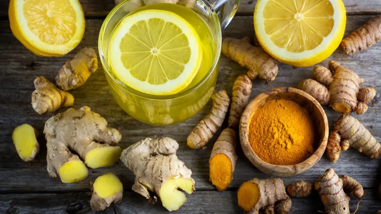 Infusión de limón y jengibre, rodeada de raíces frescas y cúrcuma en polvo. Descubre las jengibre propiedades para tu bienestar.
