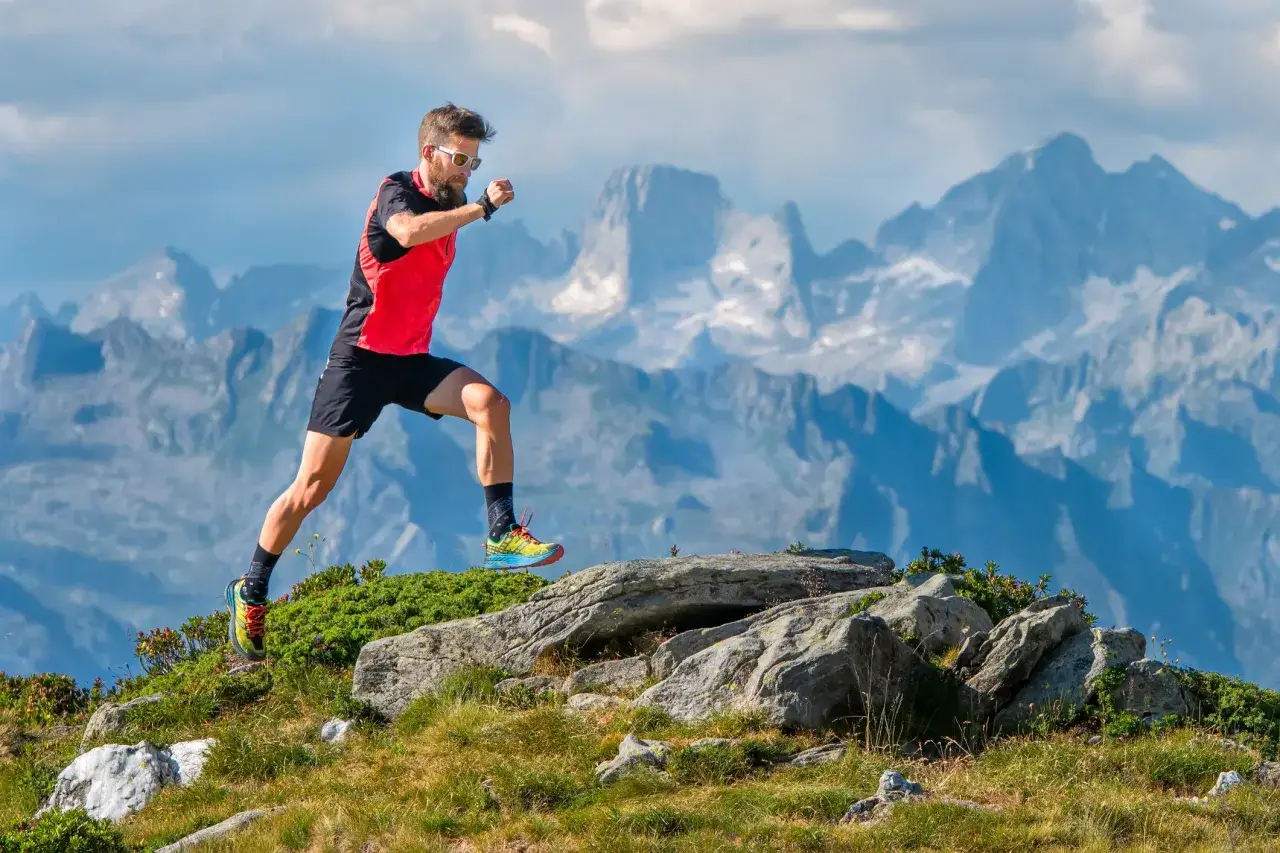 Corredor de trail running en la montaña, con un paisaje alpino de fondo. Sus movimientos sugieren ejercicios de fuerza para trail running.