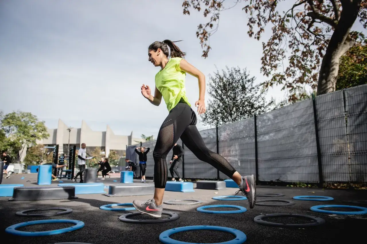Mujer entrenando al aire libre, corriendo con la regla de agilidad en el suelo.