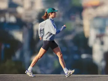 Mujer con gorra y sudadera gris corriendo al aire libre, disfrutando de un paseo después de comer para mantenerse activa.