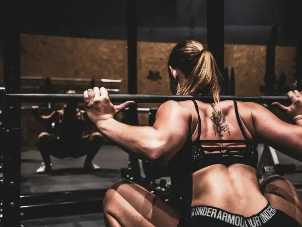 Mujer haciendo sentadillas con barra, un ejercicio clave para saber como ganar masa muscular rápido.