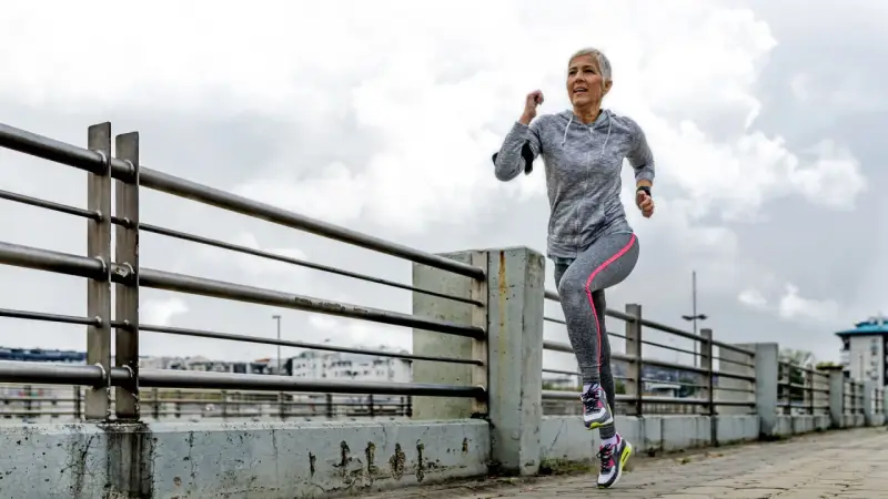 Mujer mayor corre por un paseo marítimo. ¡Una guía sobre cómo empezar a correr para principiantes!