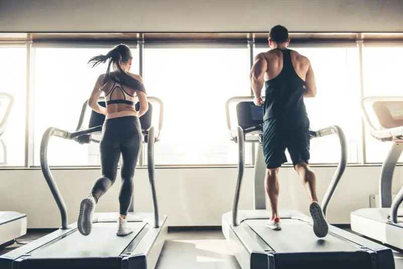 Hombre y mujer corriendo en cintas de correr, disfrutando de su rutina de cardio en ayunas.
