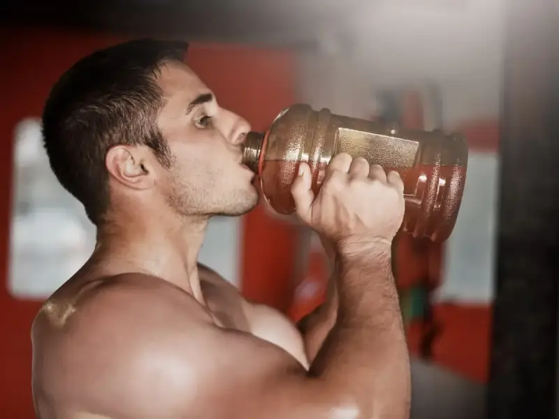 Hombre bebiendo de una botella grande, preparándose para el entrenamiento. ¿Cuántos gramos de pre entreno tomar?