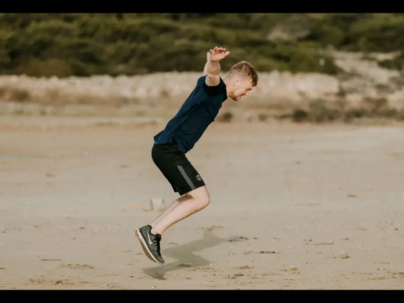 Hombre en la playa haciendo ejercicio, elevando las rodillas en un salto dinámico.