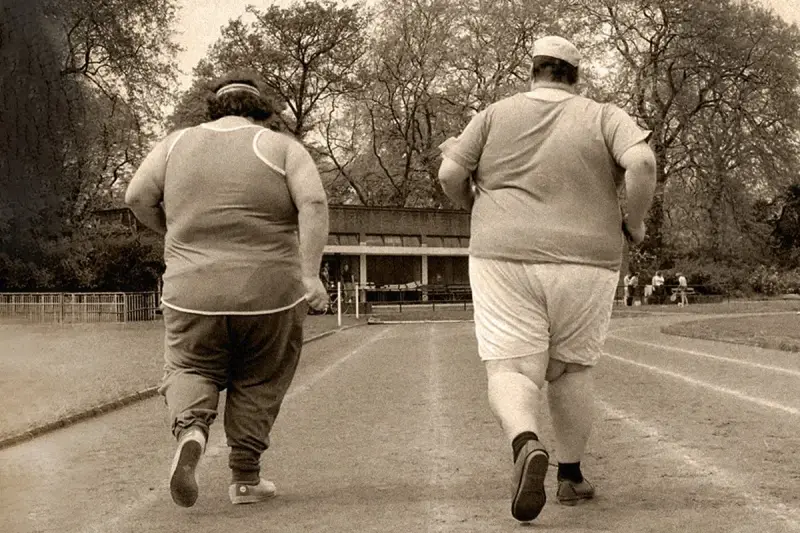 Dos personas con sobrepeso corren en una pista de atletismo. El andar adelgaza, y ellos lo saben.