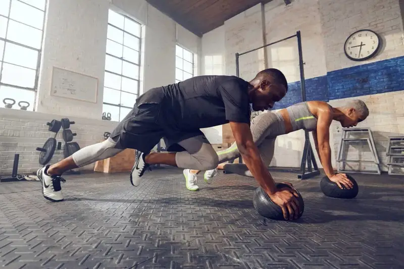 Pareja haciendo cardio en casa, en posición de plancha con balones medicinales.
