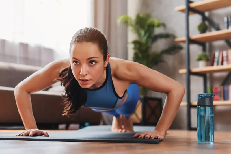 Mujer concentrada haciendo flexiones, parte de sus ejercicios de fuerza en casa.